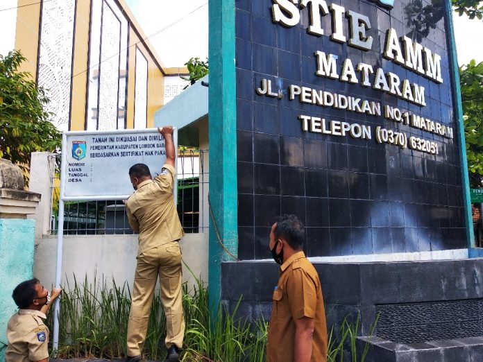 PASANG PLANG: Pihak BPKAD Lobar sedang memasang plank Barang Milik Daerah (BMD) Aset Pemkab Lobar di kampus STIE AMM Mataram Senin (7/9/2020). (Fahmy/Radar Lombok)